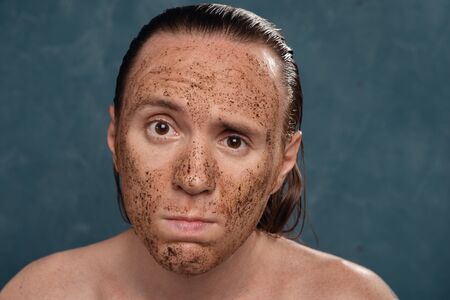 Sad man with wet long hair in coffee mask on his face waiting of the spa procedures.の写真素材