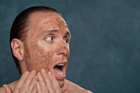 Afraid man with wet long hair in coffee mask on his face waiting of the spa procedures.の写真素材