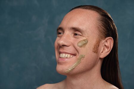 Smiling man with wet long hair in green clay mask on his face waiting of the spa proceduresの写真素材