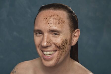 Laughing man with wet long hair in coffee mask on his face waiting of the spa procedures.の写真素材