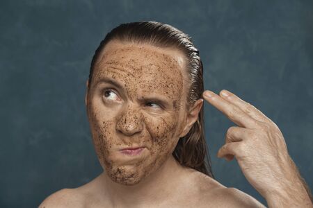 Displeased man with wet long hair in coffee mask on his face waiting of the spa procedures.の写真素材