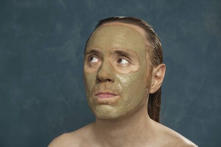 Anxious man with wet long hair in green clay mask on his face waiting of ÐµÑÑ spa procedures.の写真素材