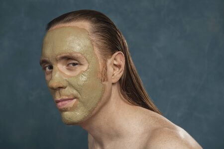Man with wet long hair in green clay mask on his face waiting of the spa procedures.の写真素材