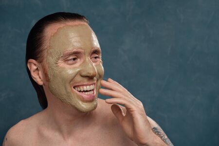Happy laughing man with wet long hair in green clay mask on his face waiting of the spa procedures.の写真素材