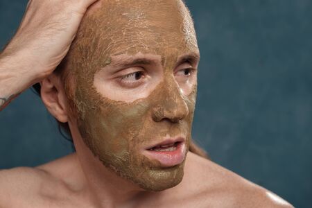 Close-up portrait of posing man with wet long hair in green clay mask on his face waiting of the spa procedures.の写真素材
