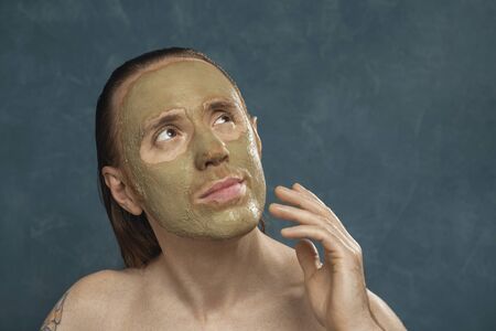 Dreaming man with wet long hair in green clay mask on his face waiting of the spa procedures.の写真素材