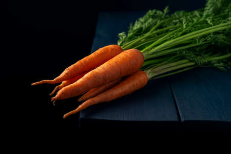 A bunch of raw carrots lies on the edge of a wooden table. Fresh vegetables on a dark background.の写真素材