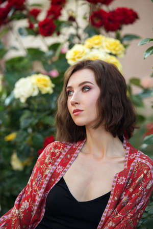 Young beautiful sexy woman posing in front of rose bush. Outdoor fashion portrait of a romantic girl with hard light.の写真素材