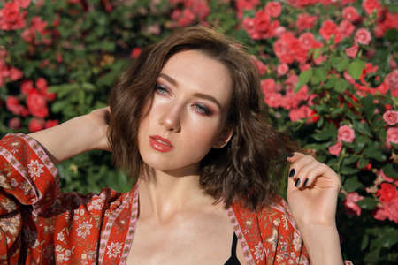 Young beautiful sexy woman posing in front of rose bush. Outdoor fashion portrait of a romantic girl with hard light.の写真素材
