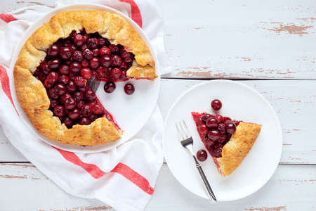Two galettes with ripe red cherry and walnut filling on dark blue background. Homemade sweet open pie with napkin and cutlery. Close-up.の写真素材