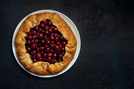Two galettes with ripe red cherry and walnut filling on dark blue background. Homemade sweet open pie with napkin and cutlery. Close-up.の写真素材