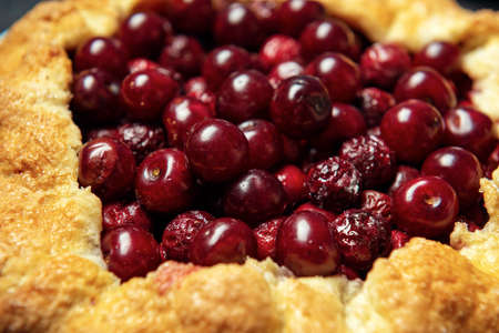 Two galettes with ripe red cherry and walnut filling on dark blue background. Homemade sweet open pie with napkin and cutlery. Close-up.の写真素材