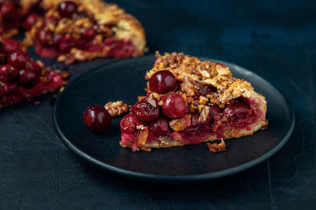 Two galettes with ripe red cherry and walnut filling on dark blue background. Homemade sweet open pie with napkin and cutlery. Close-up.の写真素材
