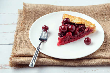 Two galettes with ripe red cherry and walnut filling on dark blue background. Homemade sweet open pie with napkin and cutlery. Close-up.の写真素材