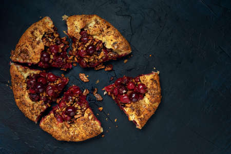 Two galettes with ripe red cherry and walnut filling on dark blue background. Homemade sweet open pie with napkin and cutlery. Close-up.の写真素材