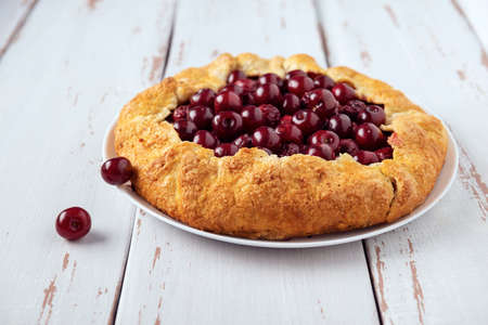 Two galettes with ripe red cherry and walnut filling on dark blue background. Homemade sweet open pie with napkin and cutlery. Close-up.の写真素材