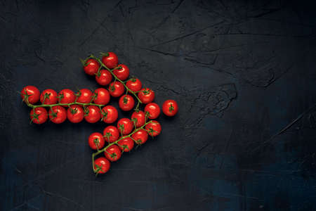 An arrow from trusses of red wet cherry tomatoes on a dark textured background. Top view. Flat lay. Space for text.の写真素材