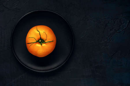 Wet yellow tomato fruit in black plate on a dark textured background. Top view. Flat lay. Space for text.の写真素材