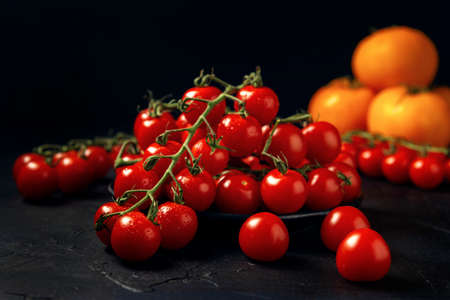 Red wet cherry tomatoes in black plate and yellow tomato fruits on a dark textured background.の写真素材