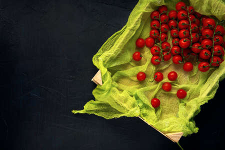A wooden box with red cherry tomatoes on dark textured table. Top view. Space for text. Flat lay.の写真素材