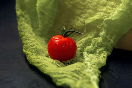 A single red wet cherry tomato on a green gauze background.の写真素材
