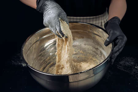 Woman in checkered apron and black gloves mixing yeast dough. Process of making bakery. The Adjarian Khachapuri Recipe â Georgian cheese bread.の写真素材