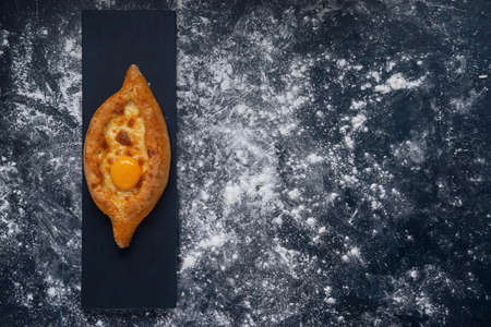 Adjarian Khachapuri â Georgian cheese bread. Baked open pie with cheese and egg yolk filling. Bakery with wheat flour on dark blue textured background. Top view. Space for text.の写真素材