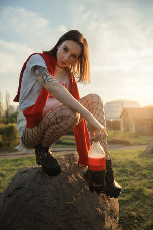 Young pretty fashion woman in fishnet tights sits on the rock. Golden hour portrait.の写真素材