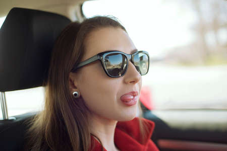 Young pretty woman shows tongue while drive a car. Positive emotions of a funny girl.の写真素材
