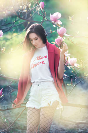 Young dreamed woman near blooming magnolia tree. Pretty fashion girl with the pink flowers.の写真素材