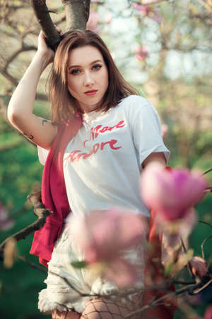 Young attractive woman near blooming magnolia tree. Pretty fashion girl with the pink flowers.の写真素材