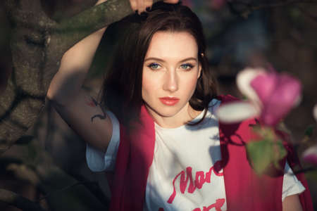 Young attractive woman posing blooming magnolia tree. Pretty fashion girl with the pink flowers.の写真素材