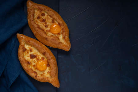 Two baked open pies with cheese and egg yolk filling on dark textured background. Adjarian Khachapuri â Georgian cheese bread. Top view. Flat lay. Space for text.の写真素材