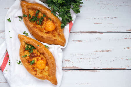 Adjarian Khachapuri â Georgian cheese bread decorated with parsley. Two baked open pies with cheese and egg yolk filling on white napkin and Provence style background. Top view. Flat lay. Space for text.の写真素材