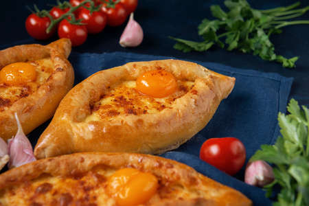 Adjarian Khachapuri â Georgian cheese bread with tomatoes, parsley and garlic on blue napkin. Baked open pie with cheese and egg yolk filling.の写真素材