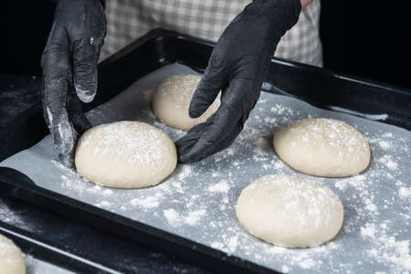 Woman in checkered apron and black gloves put a piece of yeast dough in baking tray. Process of making bakery. The Adjarian Khachapuri Recipe â Georgian cheese bread.の写真素材