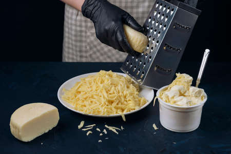 Woman in checkered apron and black gloves rubs cheese on a grater. Home cooking. The Adjarian Khachapuri Recipe â Georgian cheese bread.の写真素材