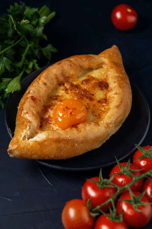 The Adjarian Khachapuri â Georgian cheese bread with tomatoes and parsley. Baked open pie with cheese and egg yolk filling.の写真素材