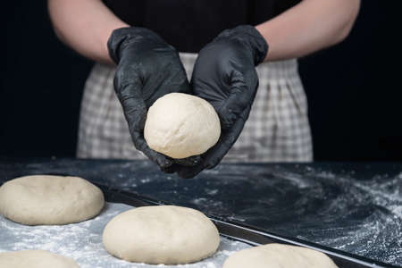 Woman in checkered apron and black gloves hold small piece of yeast dough. Process of making bakery. The Adjarian Khachapuri Recipe â Georgian cheese bread.の写真素材