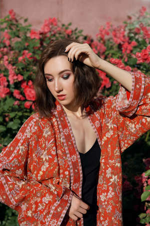 Young beautiful dreamy woman with red roses on a background. Outdoor portrait of a romantic girl with the hard sunlight.の写真素材