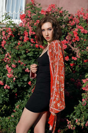 Young beautiful female posing near red roses. Outdoor portrait of a romantic woman with the hard sunlight.の写真素材