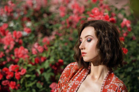 Young beautiful dreamy woman with red roses on a background. Outdoor portrait of a romantic girl with the hard sunlight. Space for text.の写真素材