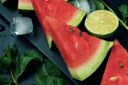 Close-up watermelon slices, mint, lime and cubes of ice on the dark textured background.の写真素材