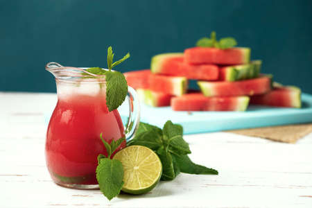 Glass jug with ice-cold watermelon juice, lime, mint and watermelon slices on the white wooden Provence style table.の写真素材
