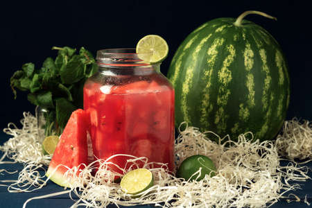 A jar with watermelon juice and whole watermelon fruit on the dark blue wooden table.の写真素材