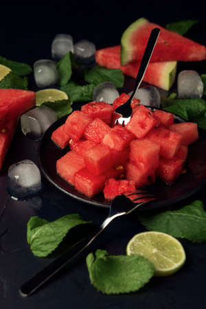 Black plate with watermelon slices, mint, lime and ice cubes on the black textured backdrop.の写真素材