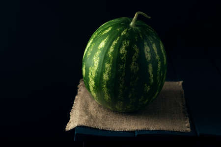 Whole green ripe watermelon on the burlap napkin and dark blue wooden table.の写真素材