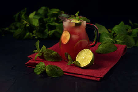 Glass jug with watermelon juice, lime and mint on red napkin and the dark textured backdrop.の写真素材