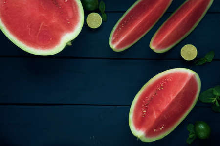 One whole watermelon with pieces of sliced one, lime and mint on the dark blue wooden table. Flat lay. Copy space. Space for text.の写真素材