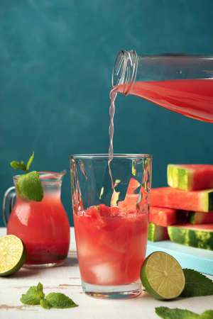 A glass with ice is filling with watermelon juice from the bottle on the white wooden Provence style table.の写真素材